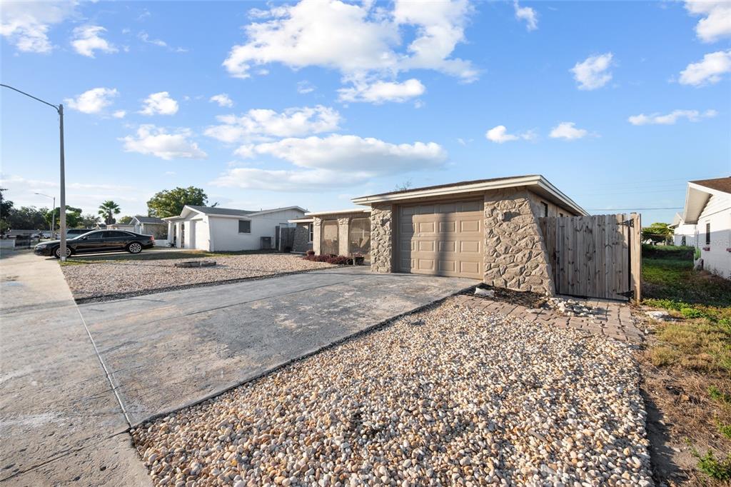 A single-story house with a stone-accented garage, concrete driveway, and gravel front yard — 5633 ANDREA DRIVE, HOLIDAY, FL
