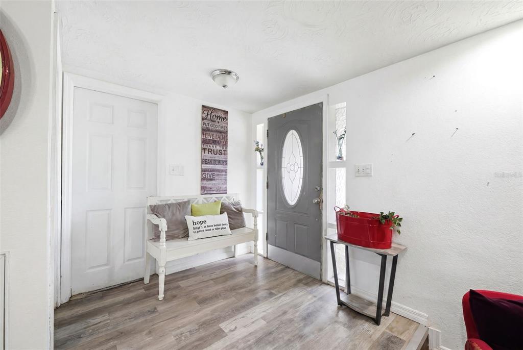 An entryway features wood-look flooring, a white bench, a gray front door, and a console table — 5633 ANDREA DRIVE, HOLIDAY, FL
