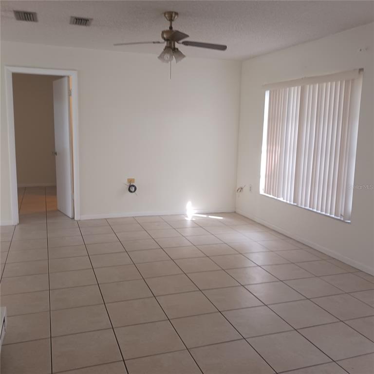 An empty room features beige tile flooring, a ceiling fan, and vertical window blinds — 3781 SW 147TH STREET, OCALA, FL