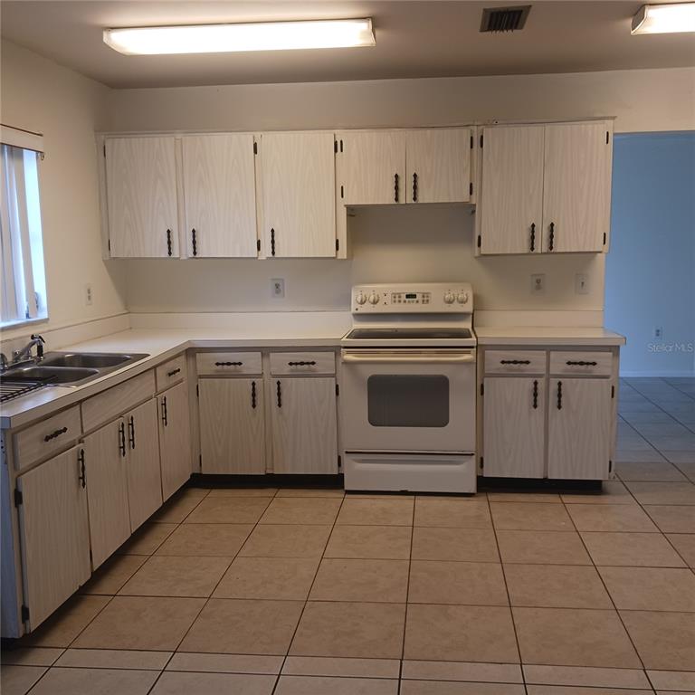 A kitchen features white cabinets, a white stove, and light-colored tile flooring — 3781 SW 147TH STREET, OCALA, FL