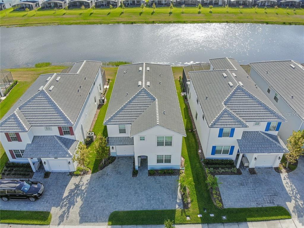 An aerial view shows three suburban houses with gray tile roofs situated along a lake — 4779 KINGS CASTLE CIRCLE, KISSIMMEE, FL
