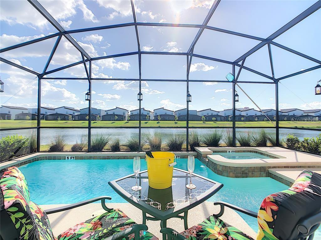 A screened-in pool and spa overlook a lake and a row of suburban houses — 4779 KINGS CASTLE CIRCLE, KISSIMMEE, FL
