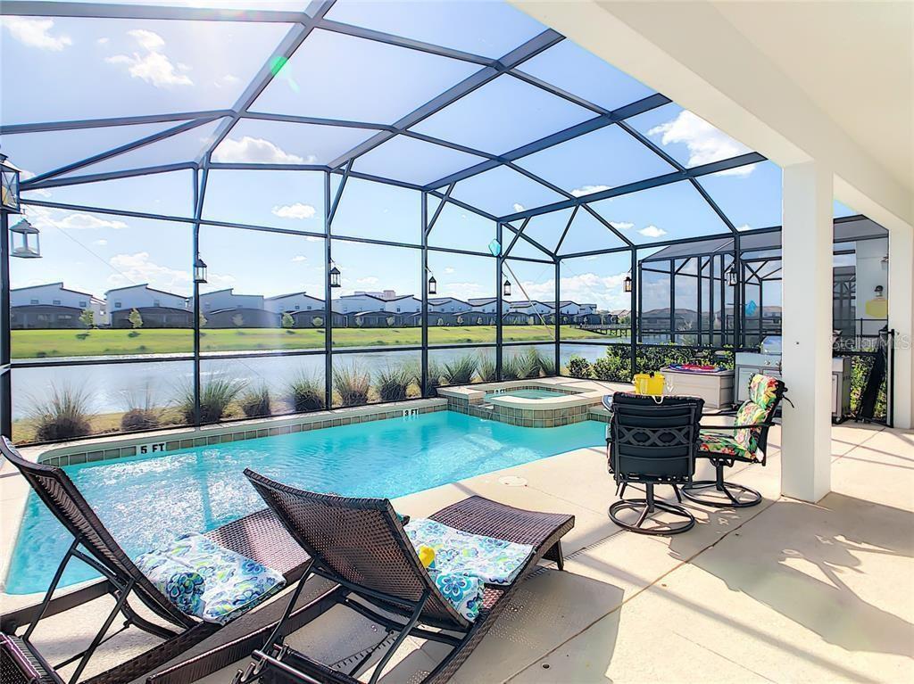 A screened-in patio features a swimming pool, a hot tub, and lounge chairs overlooking water — 4779 KINGS CASTLE CIRCLE, KISSIMMEE, FL