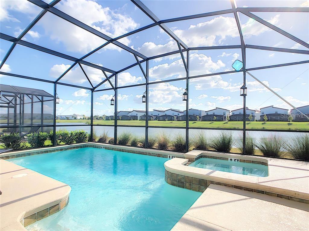 A screened-in swimming pool and spa overlook a pond and suburban houses — 4779 KINGS CASTLE CIRCLE, KISSIMMEE, FL