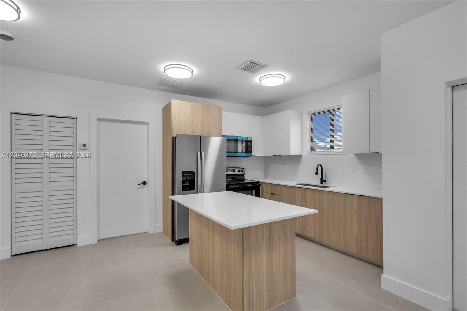 A modern kitchen features light wood cabinetry, white countertops, a central island, and stainless appliances — 6500 NW 21st Ave # 6502, Miami FL 33147, MIAMI, FL