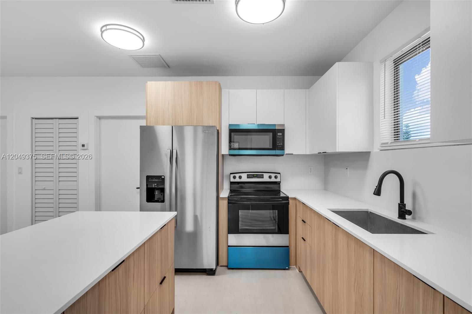 A modern kitchen features light wood cabinetry, white countertops, stainless steel appliances, and a window — 6500 NW 21st Ave # 6502, Miami FL 33147, MIAMI, FL