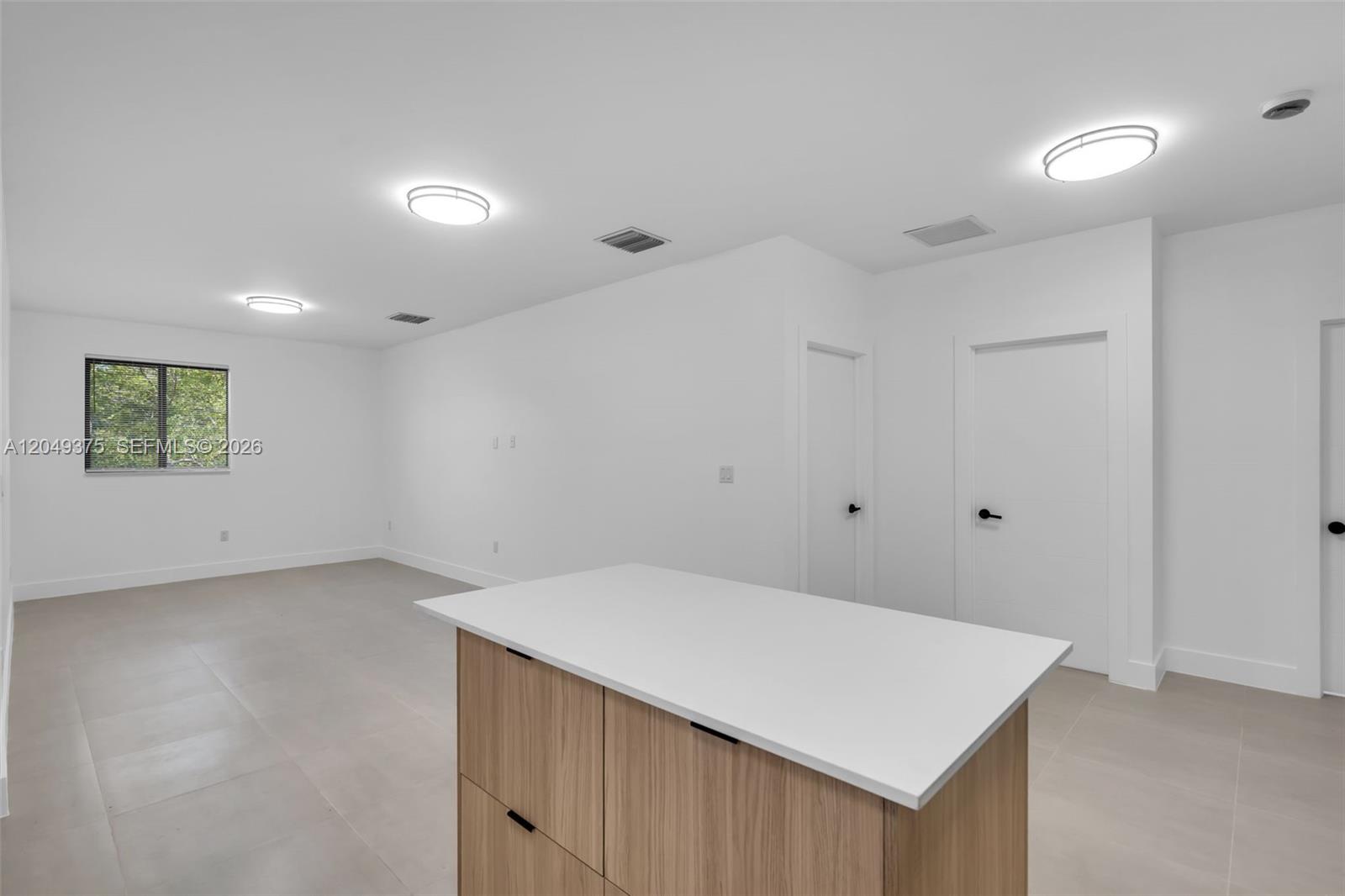 A minimalist room features light tile flooring, white walls, recessed lighting, and a wooden kitchen island — 6500 NW 21st Ave # 6502, Miami FL 33147, MIAMI, FL