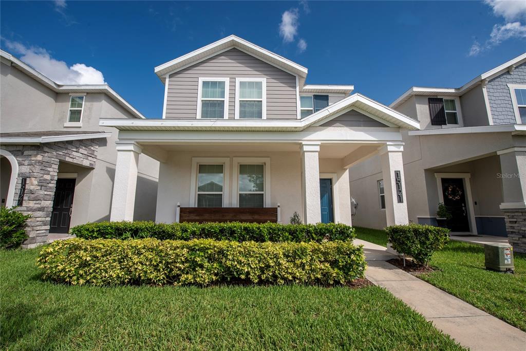 A two-story suburban house features a covered front porch, gray siding, and manicured hedges — 15121 BOOK CLUB ROAD, WINTER GARDEN, FL