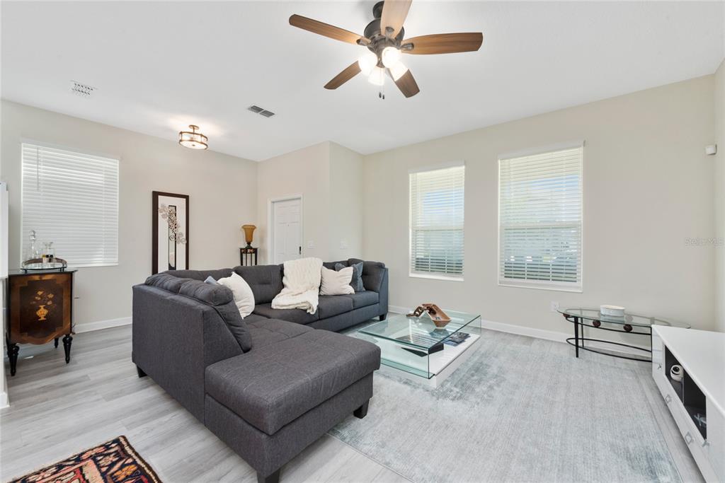 A living room features a gray sectional sofa, a glass coffee table, and light flooring — 15121 BOOK CLUB ROAD, WINTER GARDEN, FL