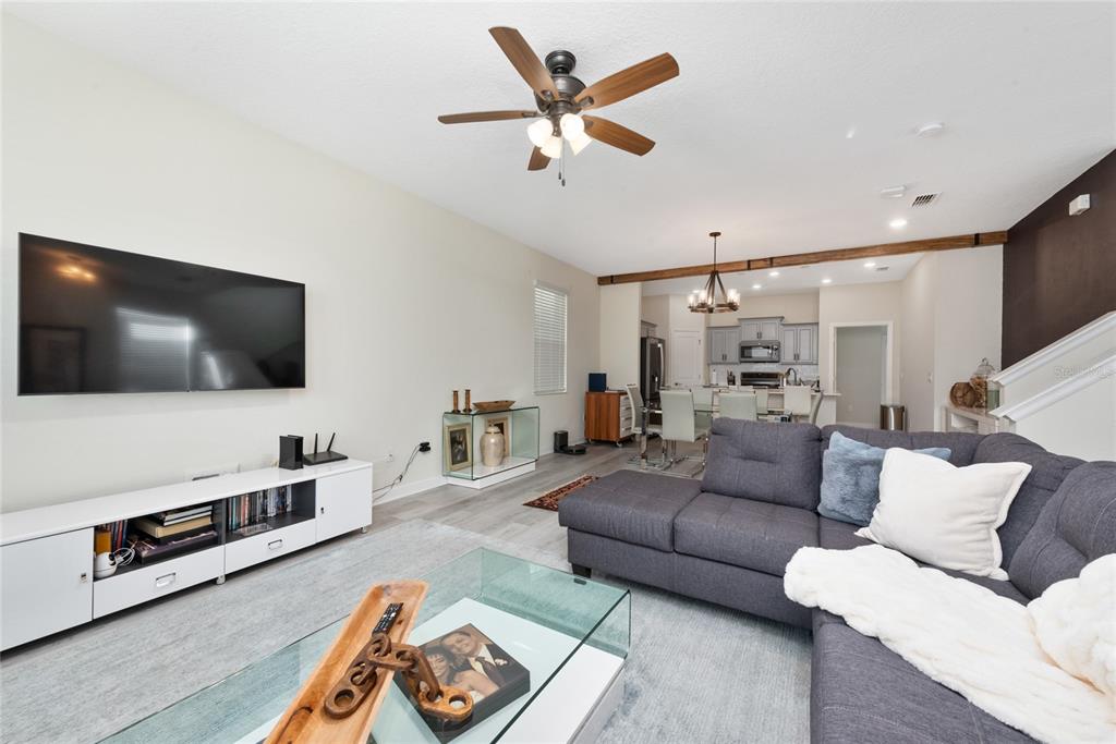 A living room with a gray sectional sofa, glass coffee table, and open-concept kitchen — 15121 BOOK CLUB ROAD, WINTER GARDEN, FL