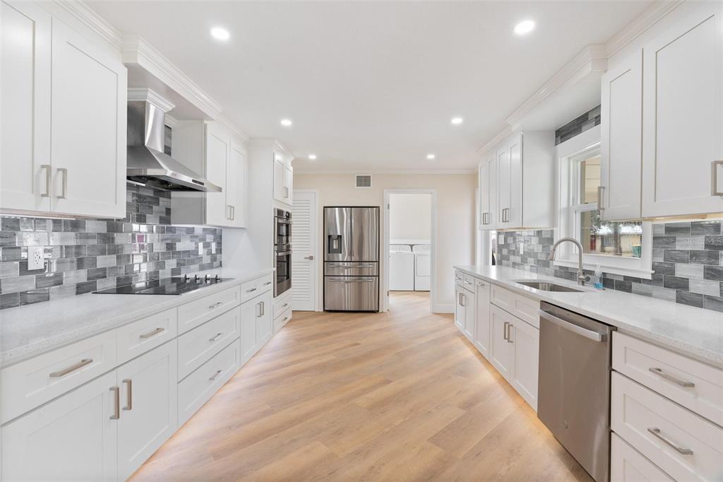 A modern kitchen features white cabinets, stainless steel appliances, quartz countertops, and a gray tile backsplash — 1310 E CROOKED LAKE DRIVE, EUSTIS, FL