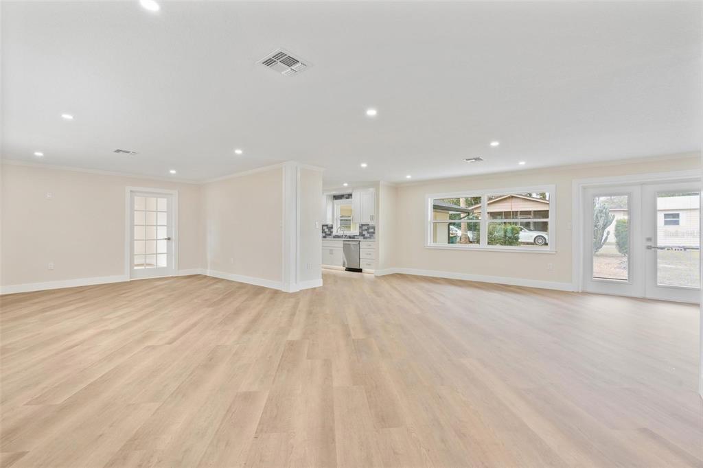 A spacious, open-concept living area features light wood-look flooring, recessed lighting, and a kitchen view — 1310 E CROOKED LAKE DRIVE, EUSTIS, FL
