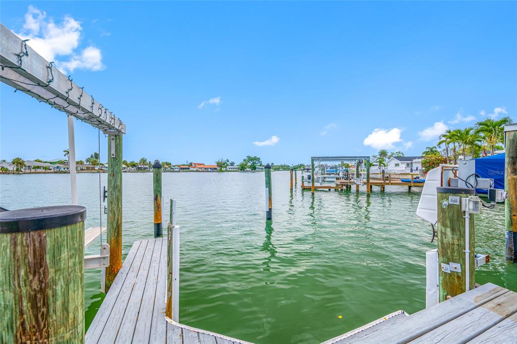 A wooden boat dock extends into a calm waterway with pilings and distant waterfront homes — 560 79TH STREET S, ST PETERSBURG, FL