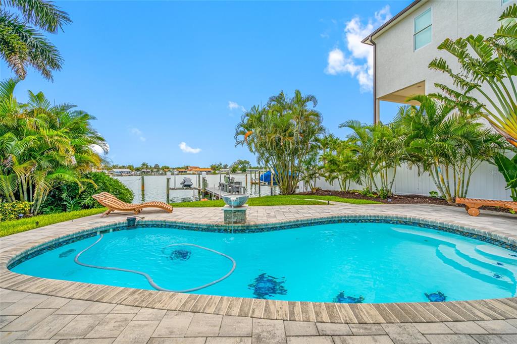A swimming pool with a fountain sits on a stone patio overlooking a canal — 560 79TH STREET S, ST PETERSBURG, FL