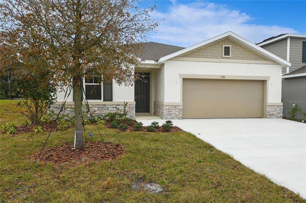 A single-story house with a tan garage, stone accents, and a front yard with a tree — 1766 CARNELIAN STREET, DELAND, FL