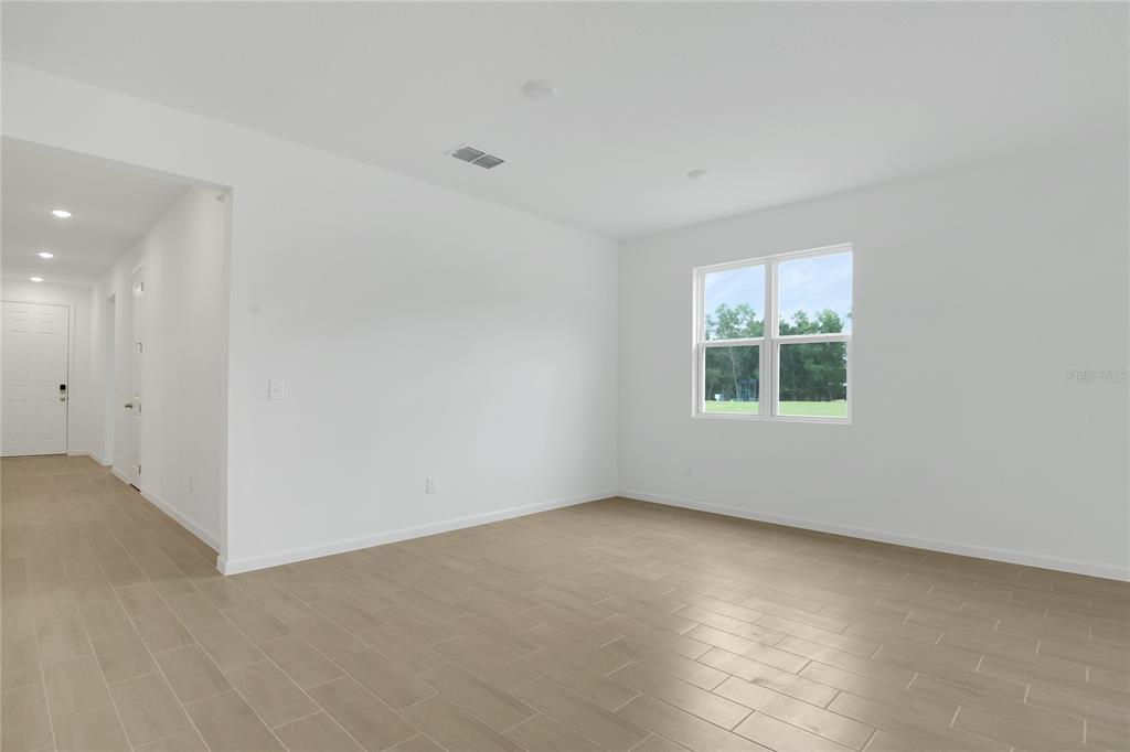 A bright, empty room features white walls, light wood-look tile flooring, and a large window — 1766 CARNELIAN STREET, DELAND, FL