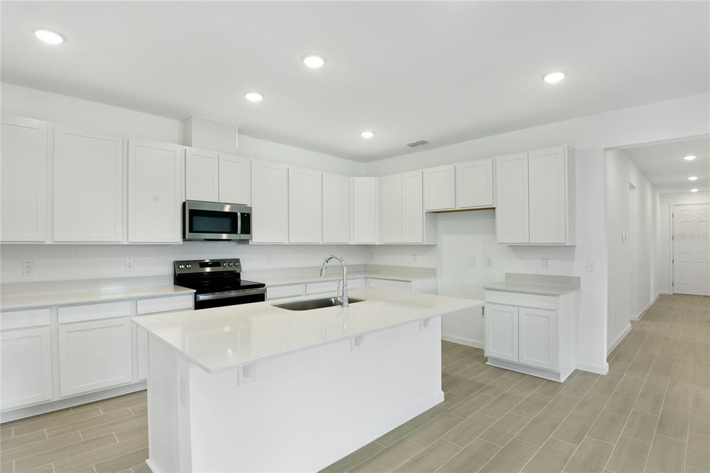 A bright kitchen features white cabinetry, a central island with a sink, and light flooring — 1766 CARNELIAN STREET, DELAND, FL