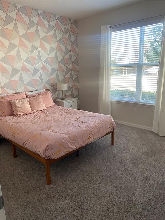 A bedroom features a geometric accent wall, a pink patterned bed, and a large window — 1523 CAREY PALM CIRCLE, KISSIMMEE, FL