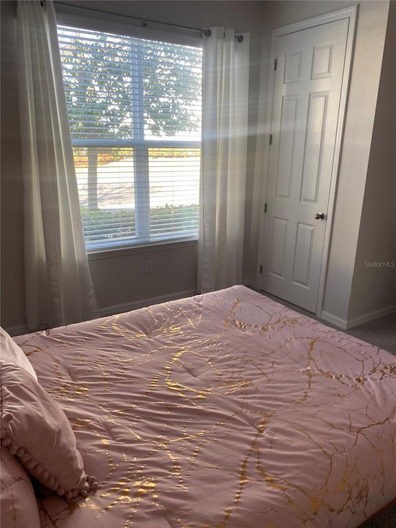 A bedroom features a bed with a pink and gold patterned comforter near a window — 1523 CAREY PALM CIRCLE, KISSIMMEE, FL