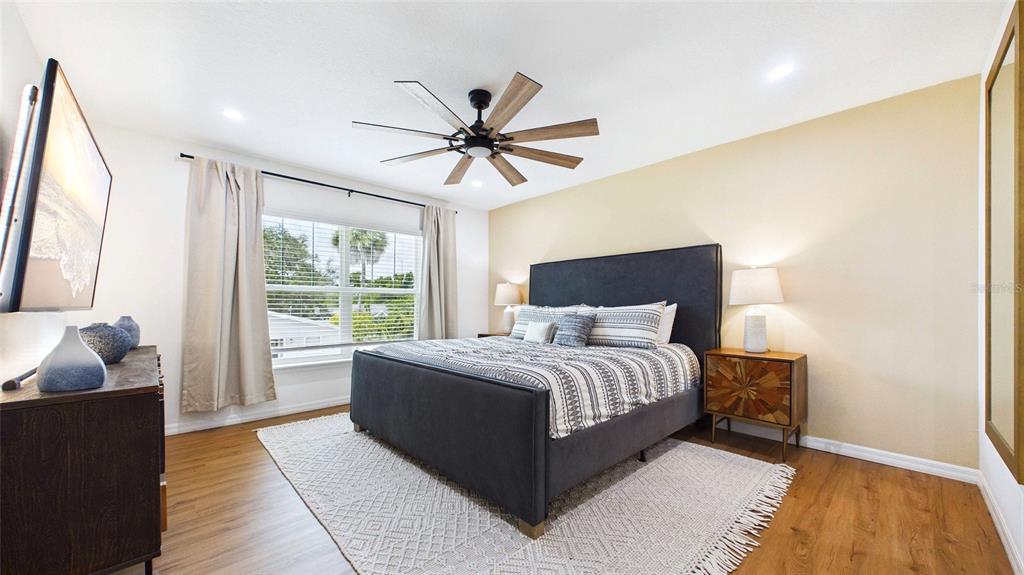 A bedroom features a dark upholstered bed, wood flooring, a ceiling fan, and beige walls — 3802 E CURTIS STREET, TAMPA, FL