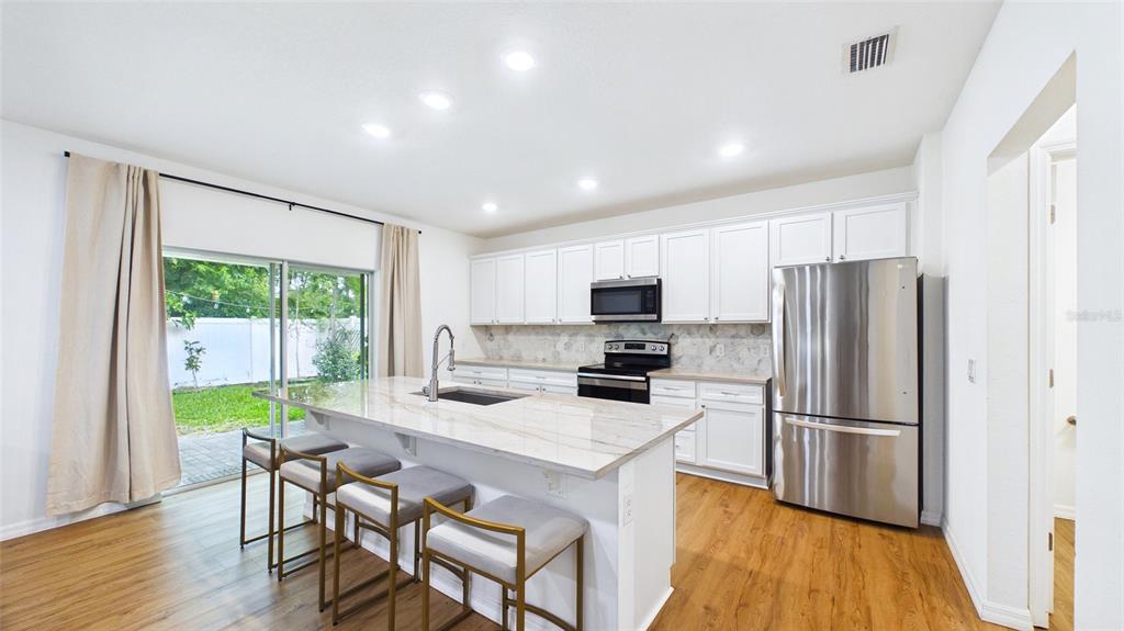 A modern kitchen features white cabinets, a marble-topped island, stainless steel appliances, and sliding doors — 3802 E CURTIS STREET, TAMPA, FL