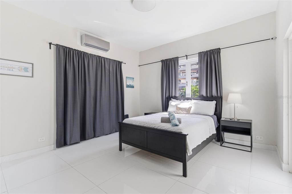 A bedroom features a black bed frame, gray curtains, white tile floors, and an air conditioner — 56 CALLE F KRUG CONDADO UNIT 3, SAN JUAN, PR
