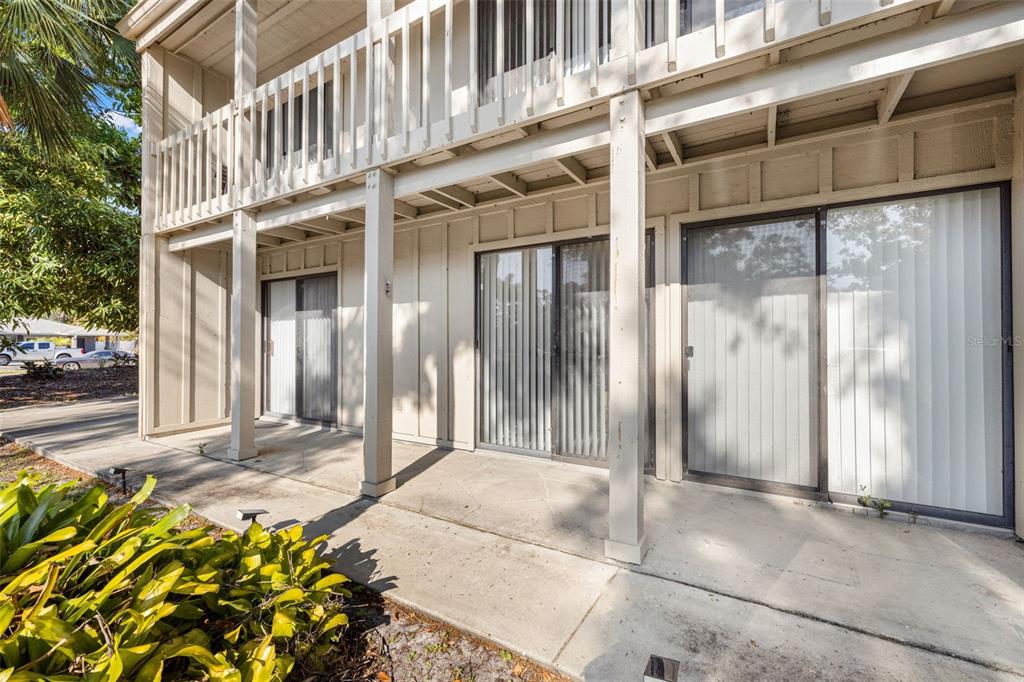 A ground-level concrete patio features two sliding glass doors under a wooden balcony structure — 2232 BAHIA VISTA STREET UNIT A1, SARASOTA, FL