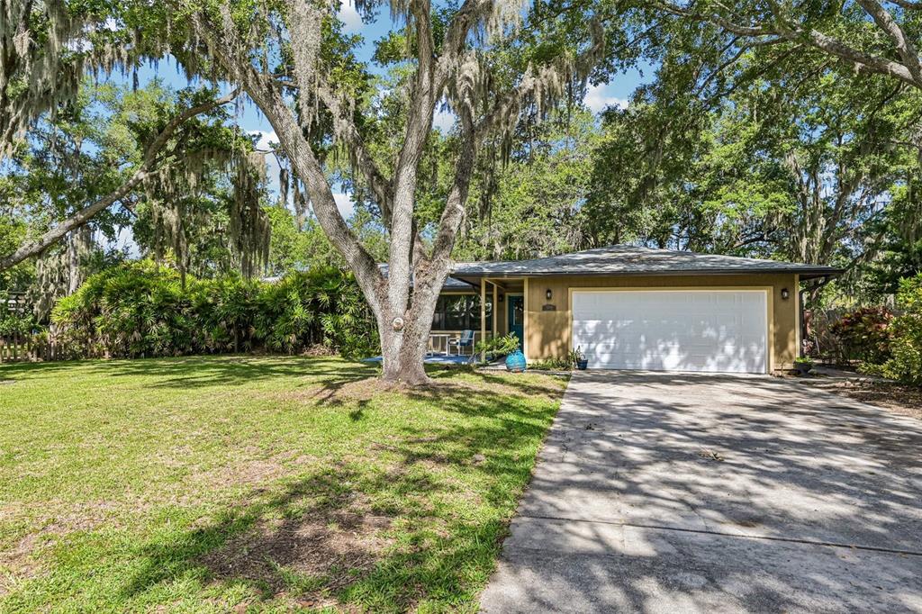 A single-story house with a white garage door, tan siding, and large mossy oak trees — 3304 SWAAN LANE, SARASOTA, FL