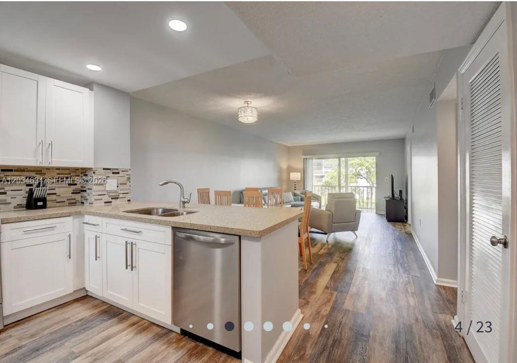A kitchen with white cabinets and a stainless steel dishwasher opens into a living area — 9880 Marina Blvd # 1516, Boca Raton FL 33428, BOCA RATON, FL