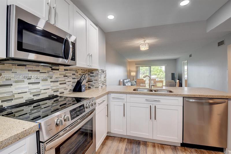 A kitchen features white cabinets, stainless steel appliances, a tiled backsplash, and a breakfast bar — 9880 Marina Blvd # 1516, Boca Raton FL 33428, BOCA RATON, FL