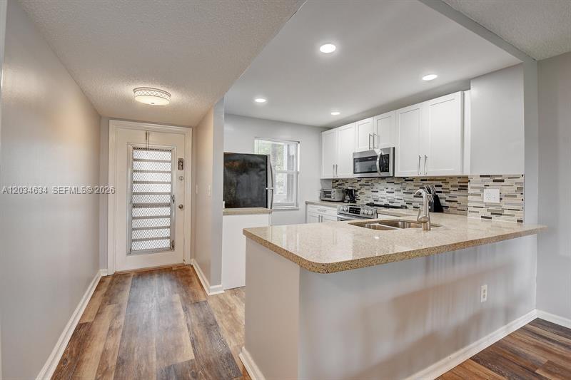 A kitchen with white cabinets, granite countertops, and a breakfast bar opens to an entryway — 9880 Marina Blvd # 1516, Boca Raton FL 33428, BOCA RATON, FL