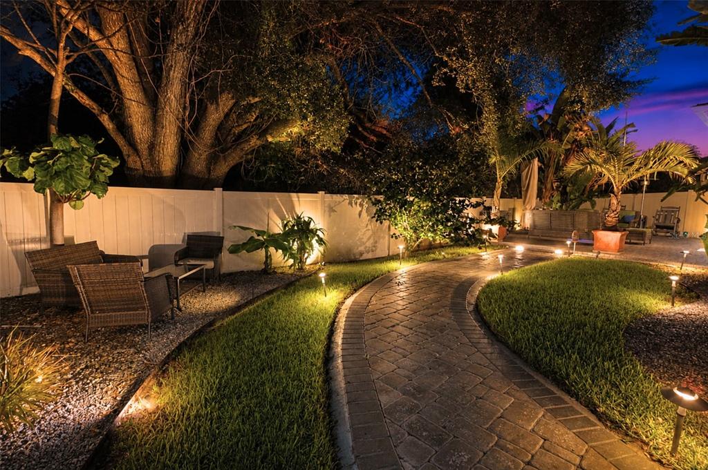 A paved stone walkway winds through a landscaped backyard illuminated by low-voltage path lighting — 842 VINO VERDE CIRCLE, BRANDON, FL