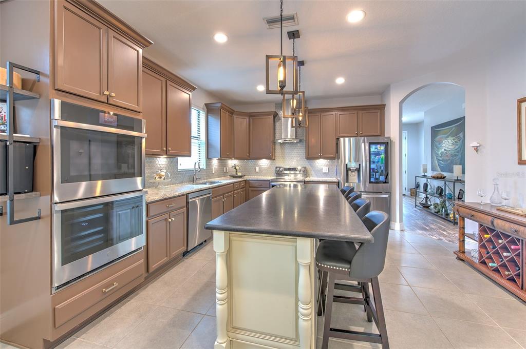 A kitchen features brown cabinetry, a large central island with seating, and stainless steel appliances — 842 VINO VERDE CIRCLE, BRANDON, FL