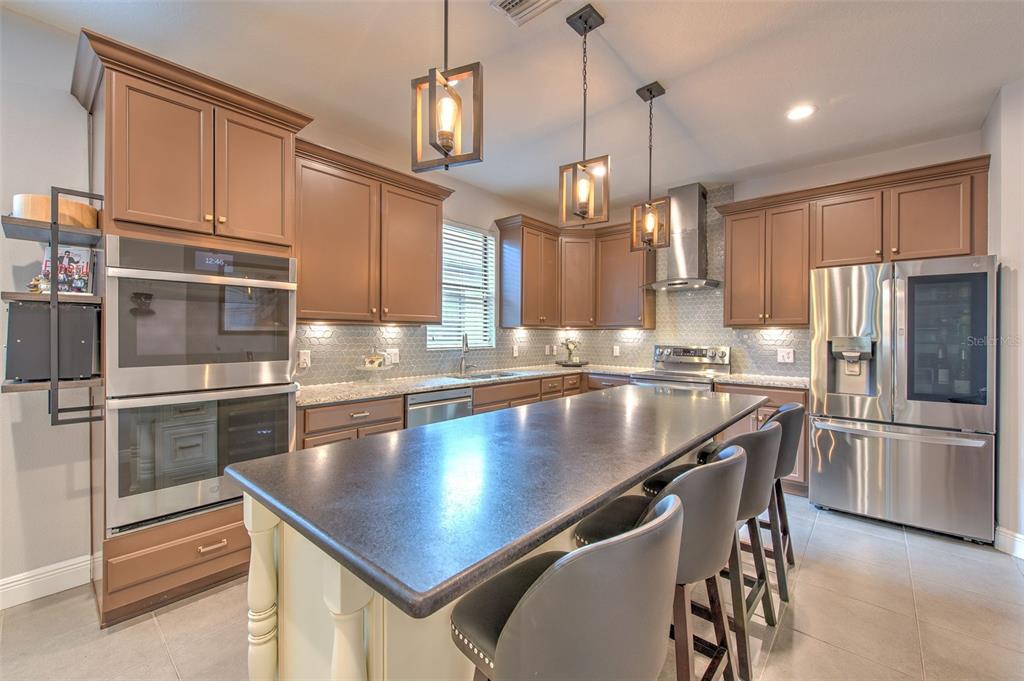 A kitchen with brown cabinets, stainless steel appliances, a dark island, and pendant lighting — 842 VINO VERDE CIRCLE, BRANDON, FL