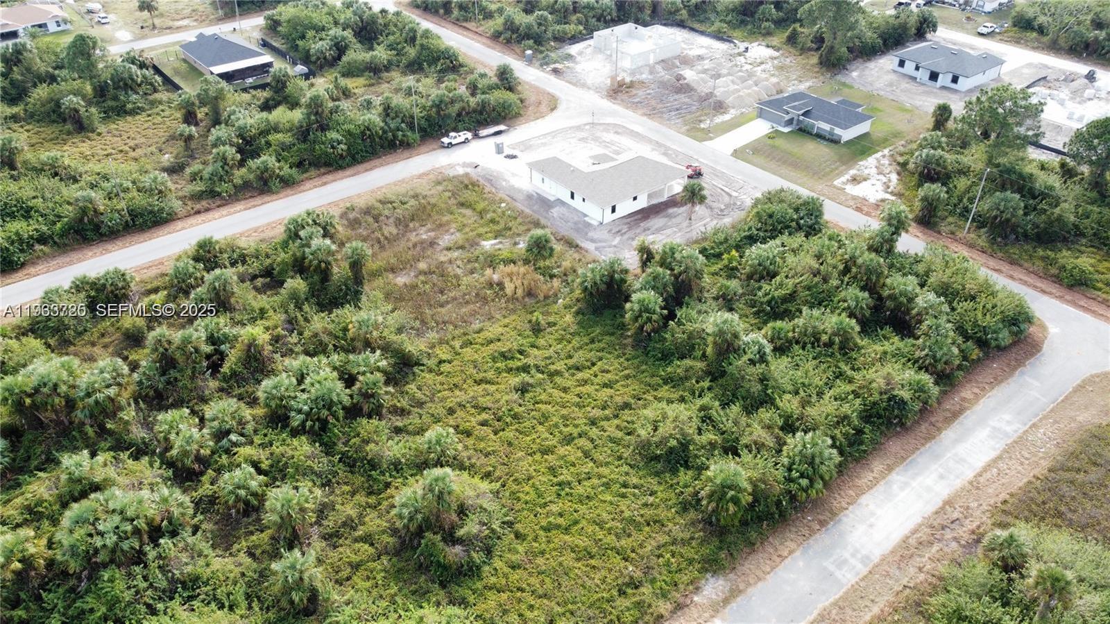 An aerial view shows a white house under construction surrounded by dense vegetation and roads — 728 Cahn St E, Lehigh Acres FL 33974, LEHIGH ACRES, FL