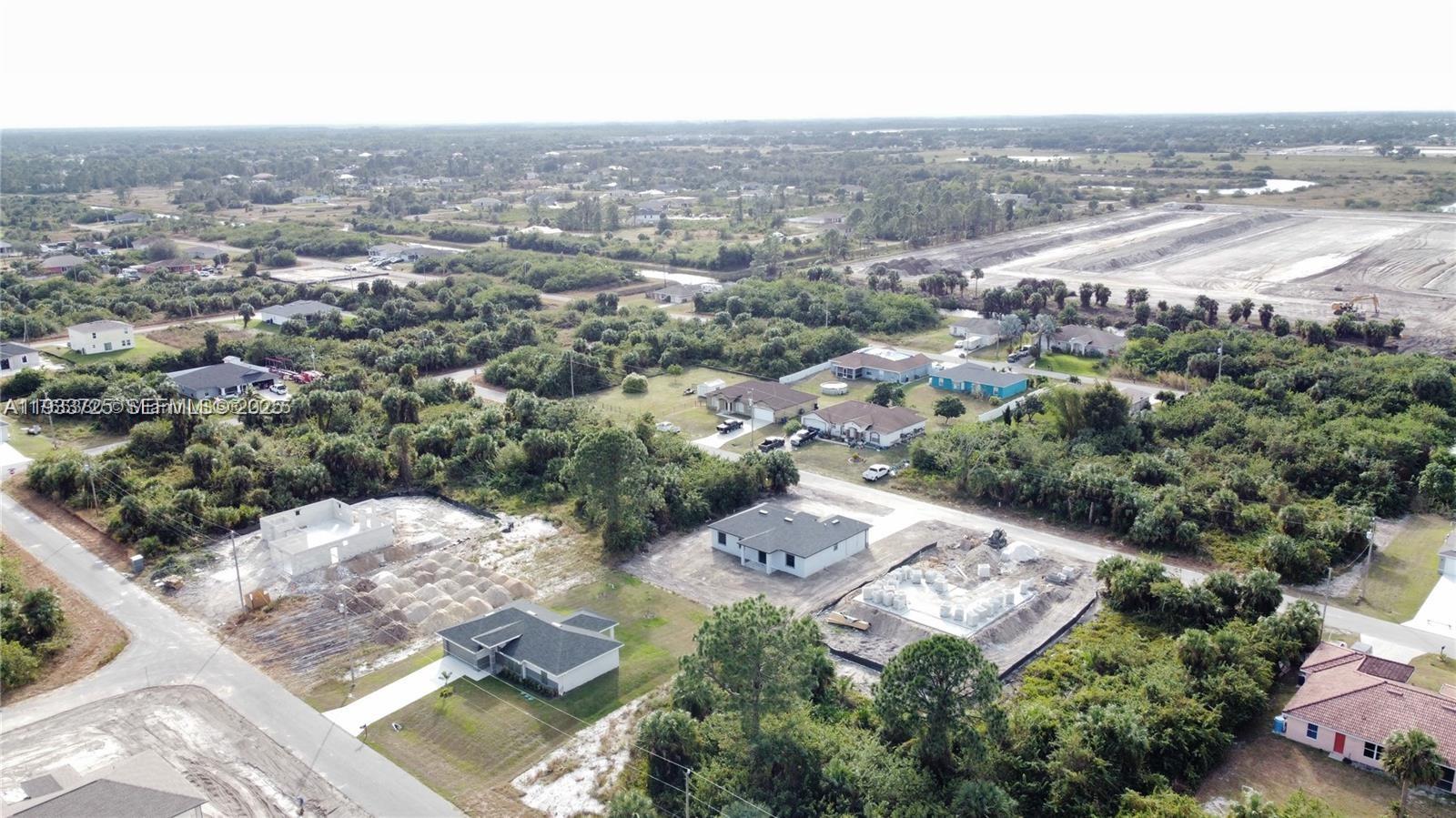 An aerial view shows several houses and construction sites in a rural, wooded area — 728 Cahn St E, Lehigh Acres FL 33974, LEHIGH ACRES, FL