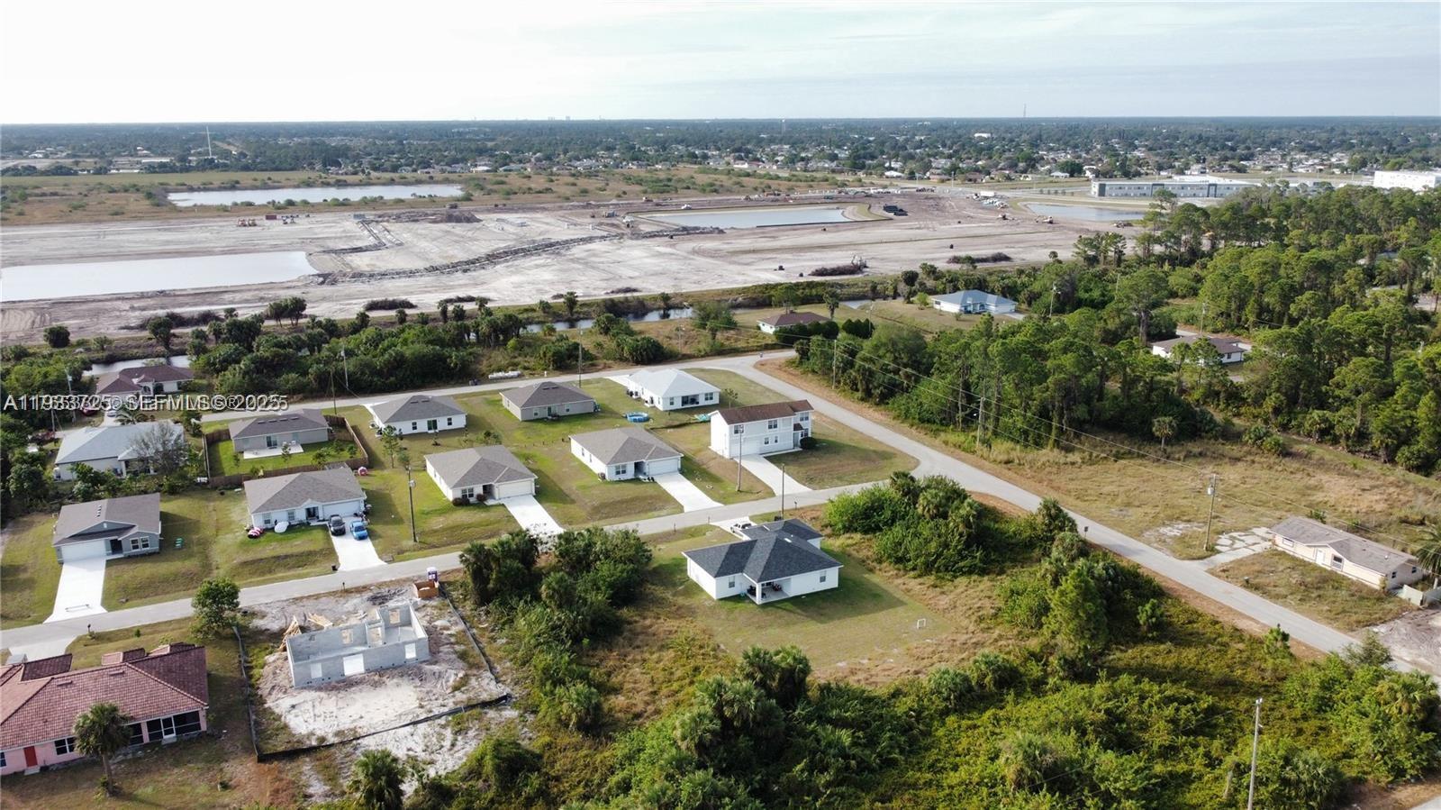 An aerial view shows a suburban neighborhood with several houses and a large construction site — 728 Cahn St E, Lehigh Acres FL 33974, LEHIGH ACRES, FL