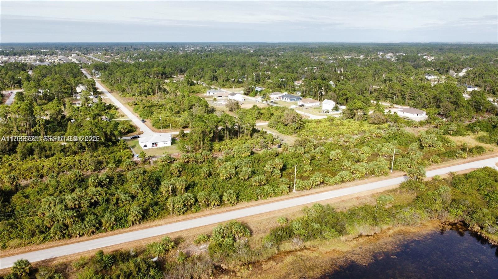 An aerial view shows a white house surrounded by dense vegetation and a paved road — 728 Cahn St E, Lehigh Acres FL 33974, LEHIGH ACRES, FL