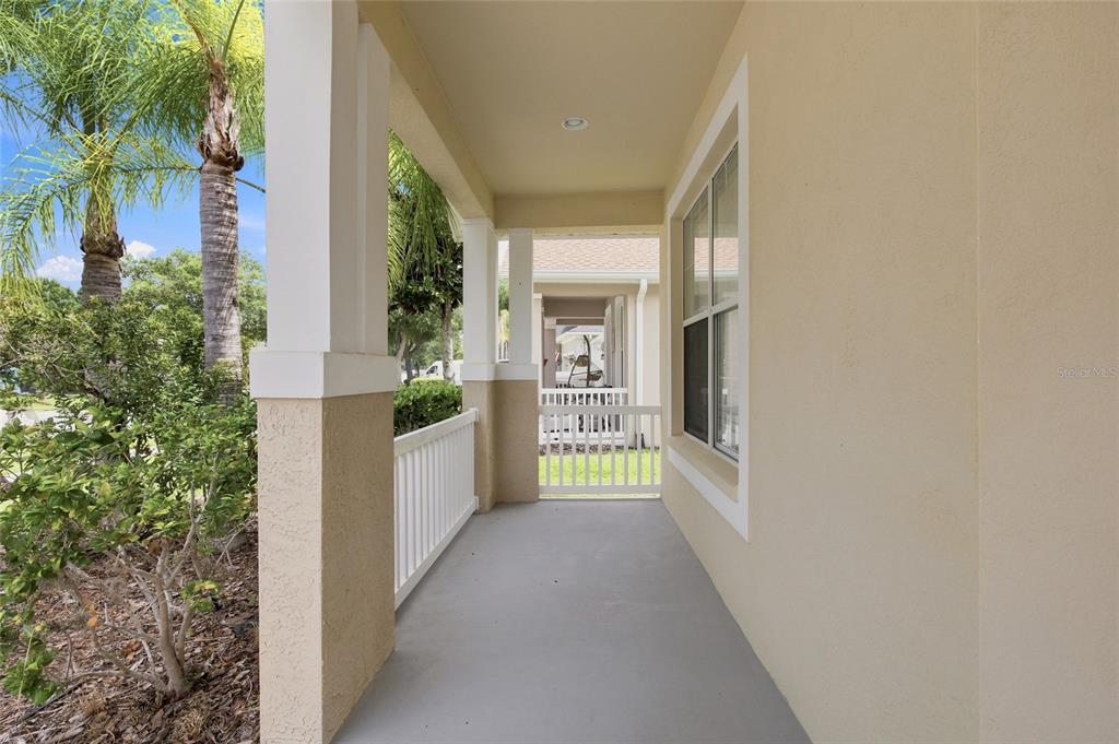 A covered porch with a white railing, beige walls, and a gray concrete floor — 7806 GRASMERE DRIVE, LAND O LAKES, FL