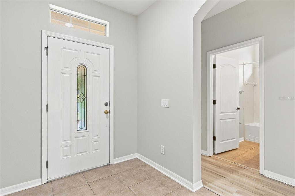 An entryway with a white front door, tile flooring, and a doorway leading to a bathroom — 7806 GRASMERE DRIVE, LAND O LAKES, FL