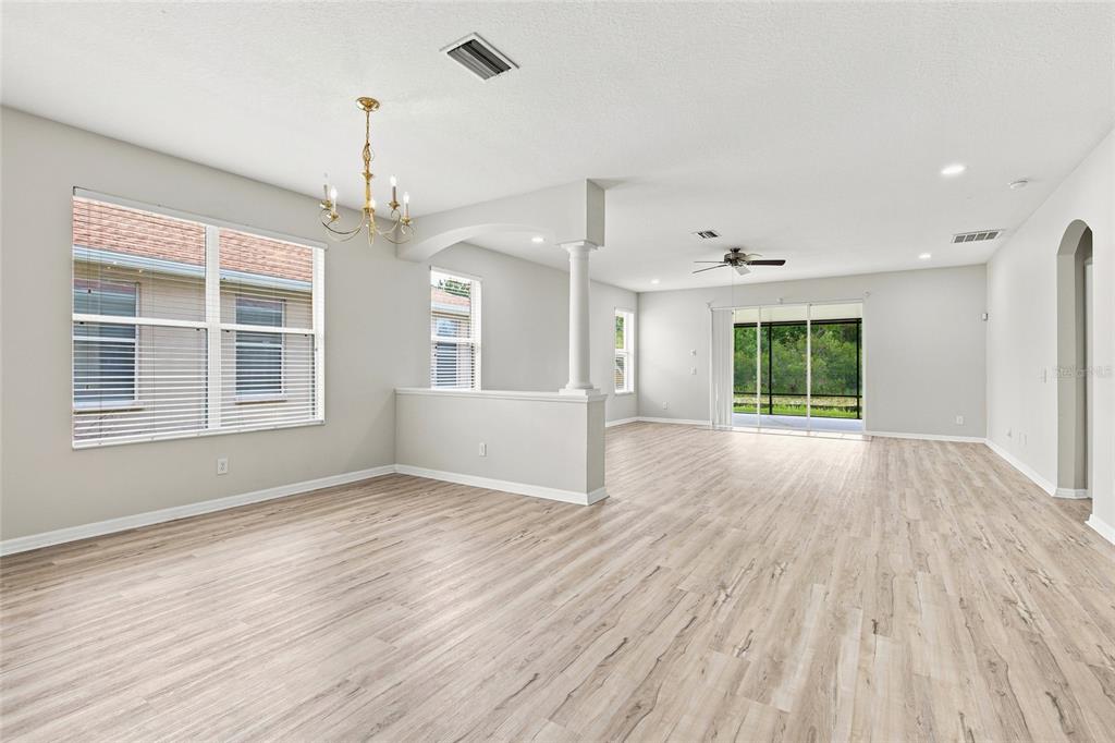 An open-concept living area features light wood-look flooring, a central column, and a dining chandelier — 7806 GRASMERE DRIVE, LAND O LAKES, FL