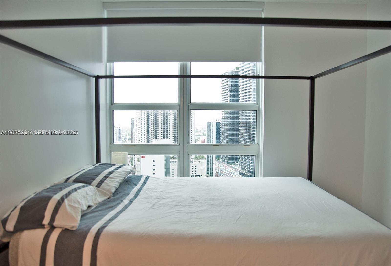 A bedroom features a canopy bed facing a large window with a city skyline view — 951 Brickell Ave # 3007, Miami FL 33131, MIAMI, FL