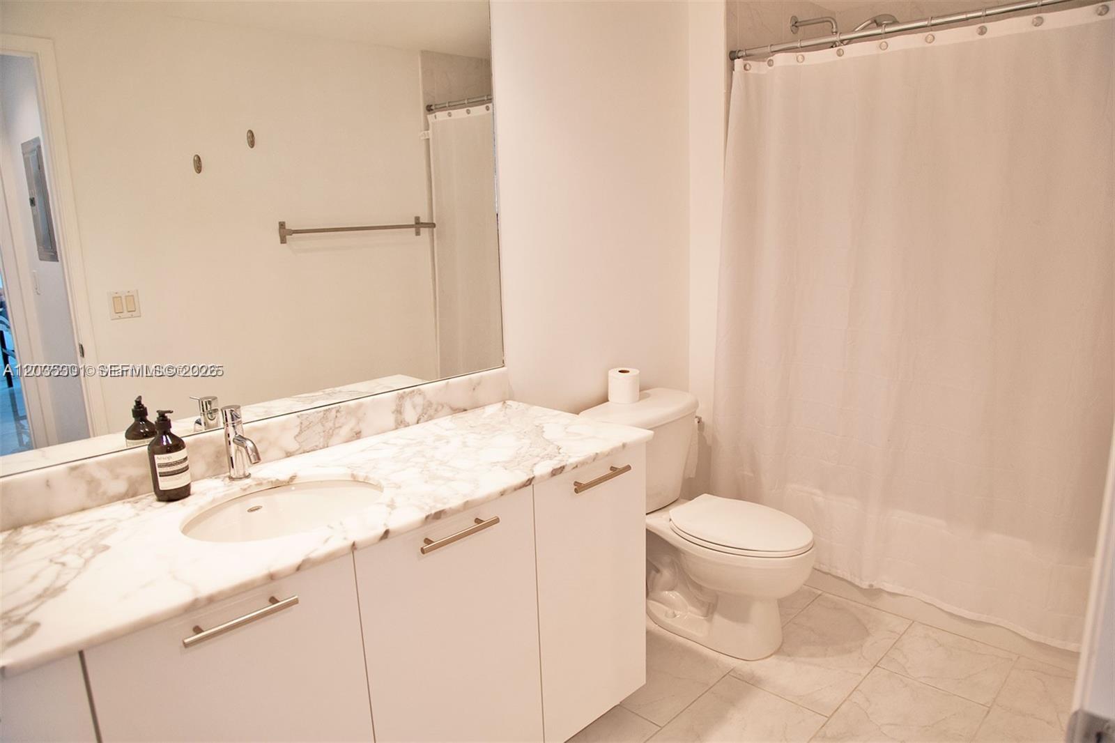 A bathroom features a marble-topped vanity, a white toilet, and a shower with a curtain — 951 Brickell Ave # 3007, Miami FL 33131, MIAMI, FL