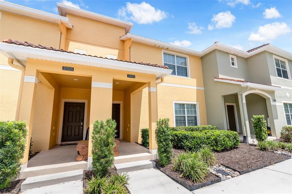 The exterior of two adjacent two-story townhomes with yellow and olive-green stucco facades — 2903 BANANA PALM DRIVE, KISSIMMEE, FL