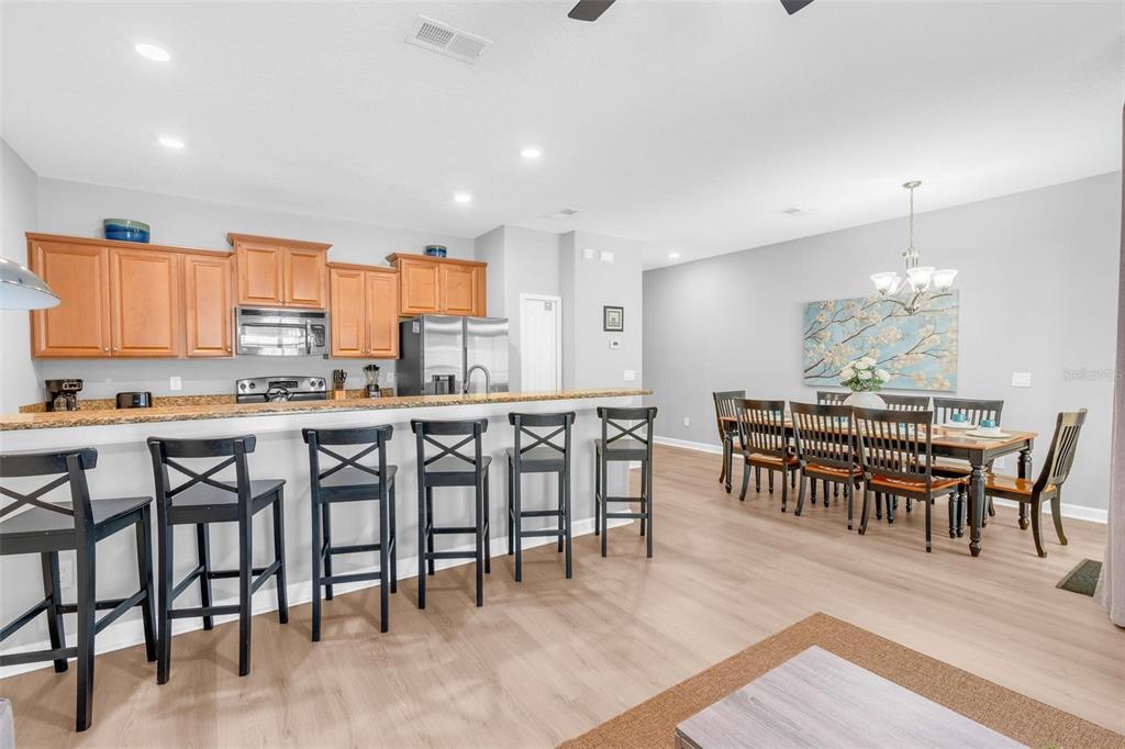 An open-concept kitchen and dining area features wood cabinets, granite countertops, and black bar stools — 2903 BANANA PALM DRIVE, KISSIMMEE, FL