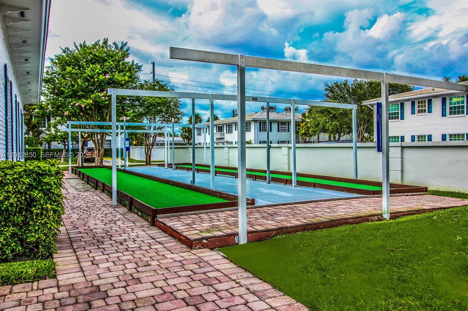 An outdoor bocce ball court with a metal frame structure sits beside a brick walkway — FORT LAUDERDALE, FL