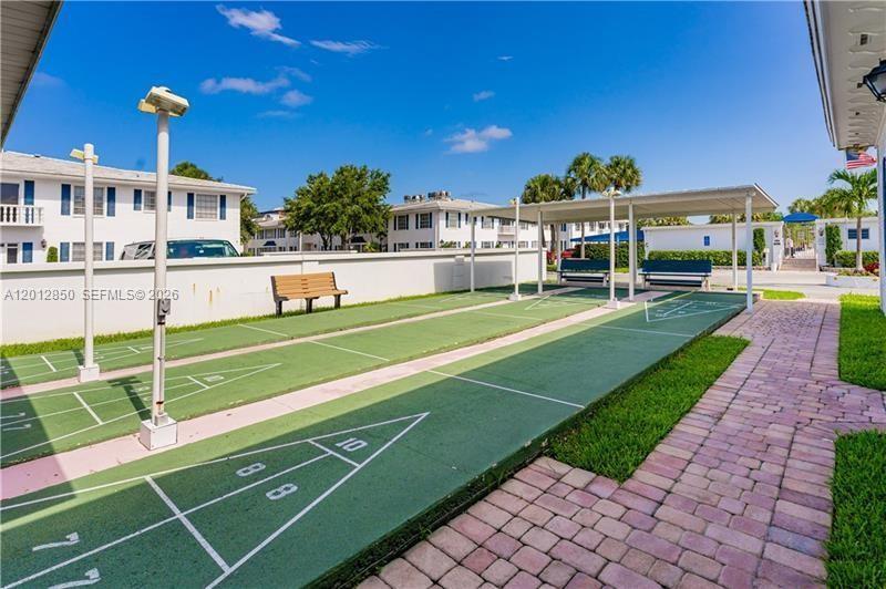 An outdoor shuffleboard court is located between a residential building and a covered seating area — FORT LAUDERDALE, FL