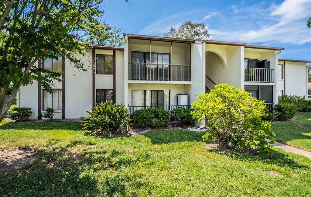 A two-story apartment building with screened balconies, white stucco walls, and surrounding landscaping — 2522 PINE RIDGE WAY S UNIT A2, PALM HARBOR, FL
