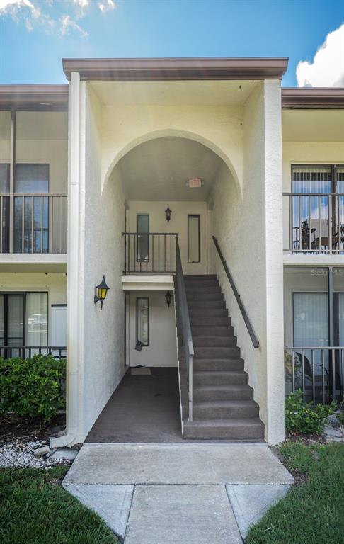 An exterior view of a multi-story apartment building featuring a central arched staircase and balconies — 2522 PINE RIDGE WAY S UNIT A2, PALM HARBOR, FL
