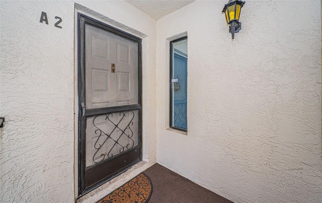 An exterior view of a front entryway featuring a screen door and a side window — 2522 PINE RIDGE WAY S UNIT A2, PALM HARBOR, FL